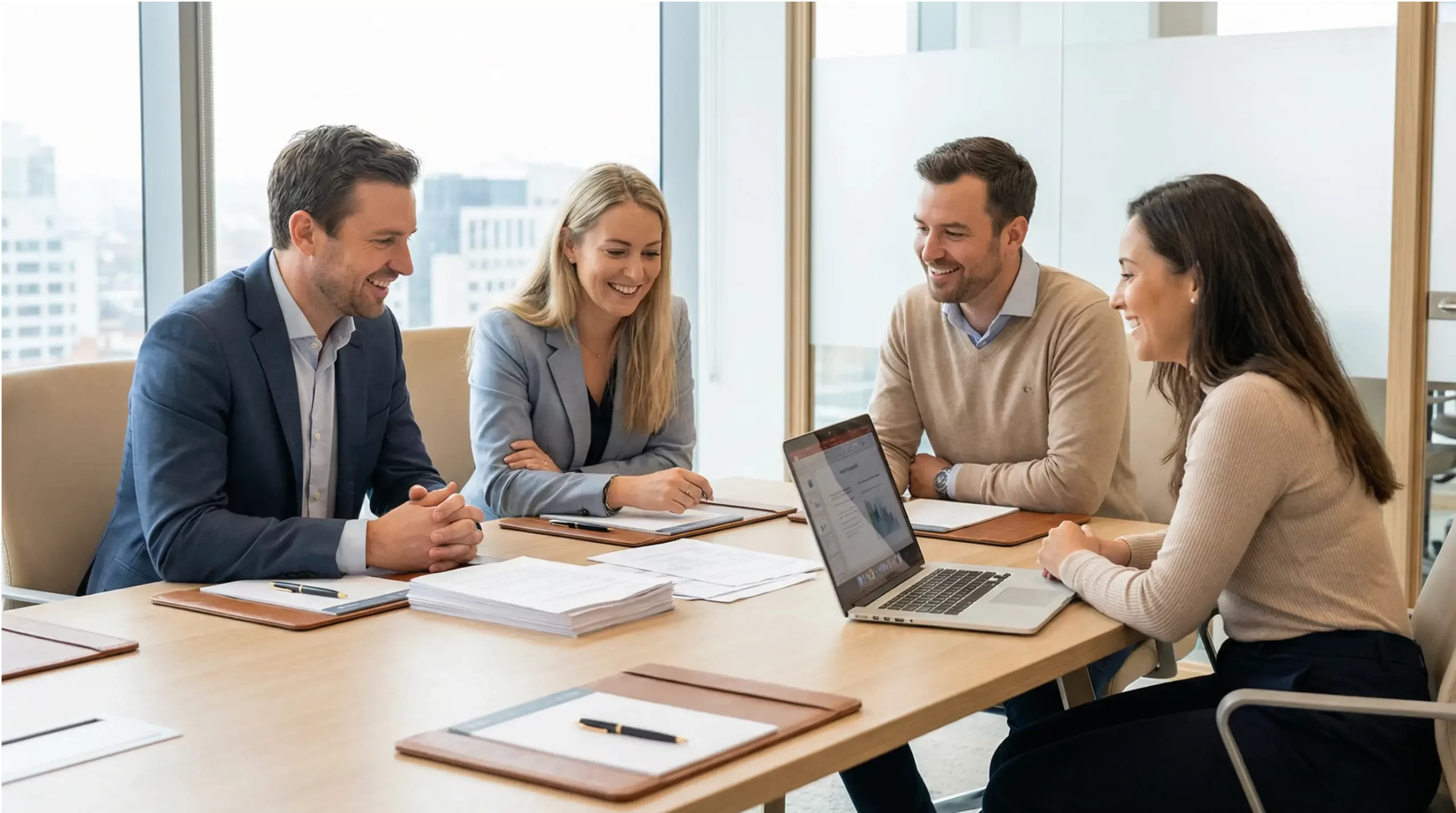 Four professionals engaged in a collaborative divorce meeting around a conference table with documents and laptop in a naturally-lit office, demonstrating the team-based approach to divorce resolution