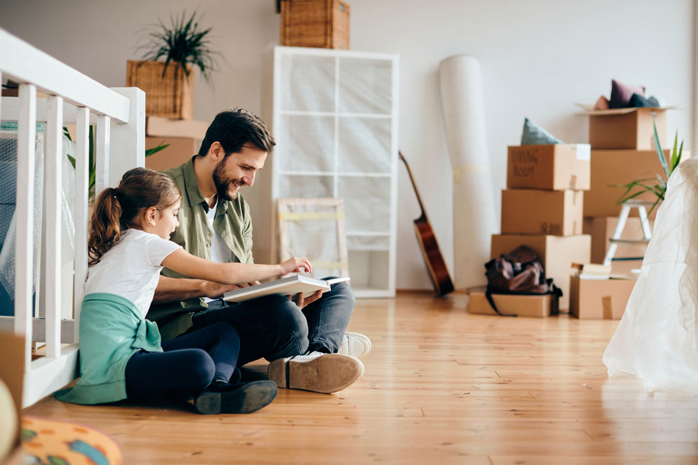 Happy father and daughter reading book while relaxing on the floor at their new home